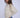 Woman wearing a cream knit sweater and blue jeans against a white background.