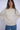 Woman wearing a cream knit sweater and blue jeans against a white background.