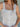 Close-up image of a woman wearing a white tank top with lace detailing.