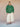 Person wearing a green cardigan and white pants against a beige background