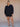 Woman wearing a black v-neck sweater and matching black knit shorts on a tan fabric backdrop.