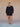 Woman wearing a black v-neck sweater and matching black knit shorts on a tan fabric backdrop.