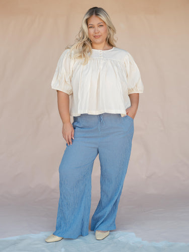 Woman wearing a cream blouse and blue plaid pants against a tan fabric background.