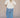Woman wearing a cream blouse and blue plaid pants against a tan fabric background.