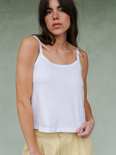 Woman wearing a white tank top and yellow pants on a plain background.