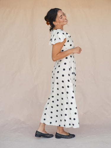 Woman wearing a white dress with black polka dots against a beige background