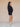 Woman wearing a black v-neck sweater and matching black knit shorts on a tan fabric backdrop.