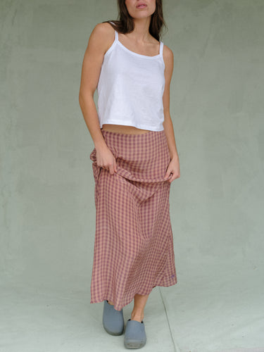 Woman wearing a white tank top and pink gingham skirt against a green background.