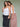 Two women hugging against a green backdrop. The woman on the left is wearing a white tank top and navy blue floral skirt, the other is wearing a white tank top and pink gingham skirt.