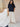 Woman wearing a navy blue t-shirt and white pants standing in front of a beige background