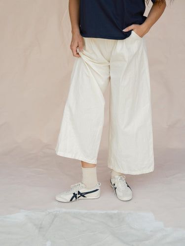 Person wearing white wide-leg pants, a navy shirt, and white sneakers on a beige background