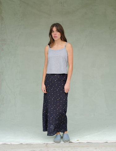 Woman wearing a heather grey tank top and navy blue floral skirt against a green background.