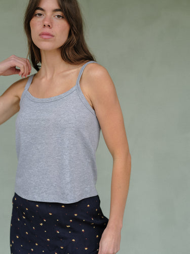 Woman wearing a heather grey tank top and navy blue floral skirt on a plain background.
