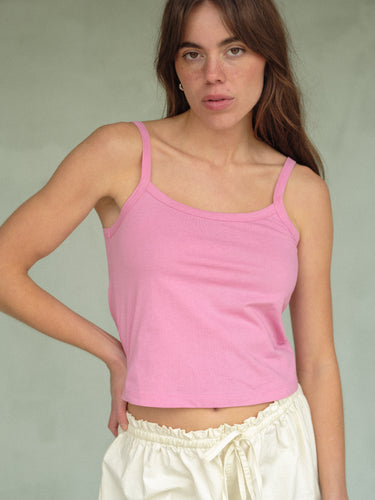 Woman wearing a pink tank top and cream shorts on a plain background.