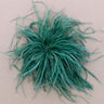 A fluffy, feathery green decorative brooch, photographed from directly above on a plain beige background.