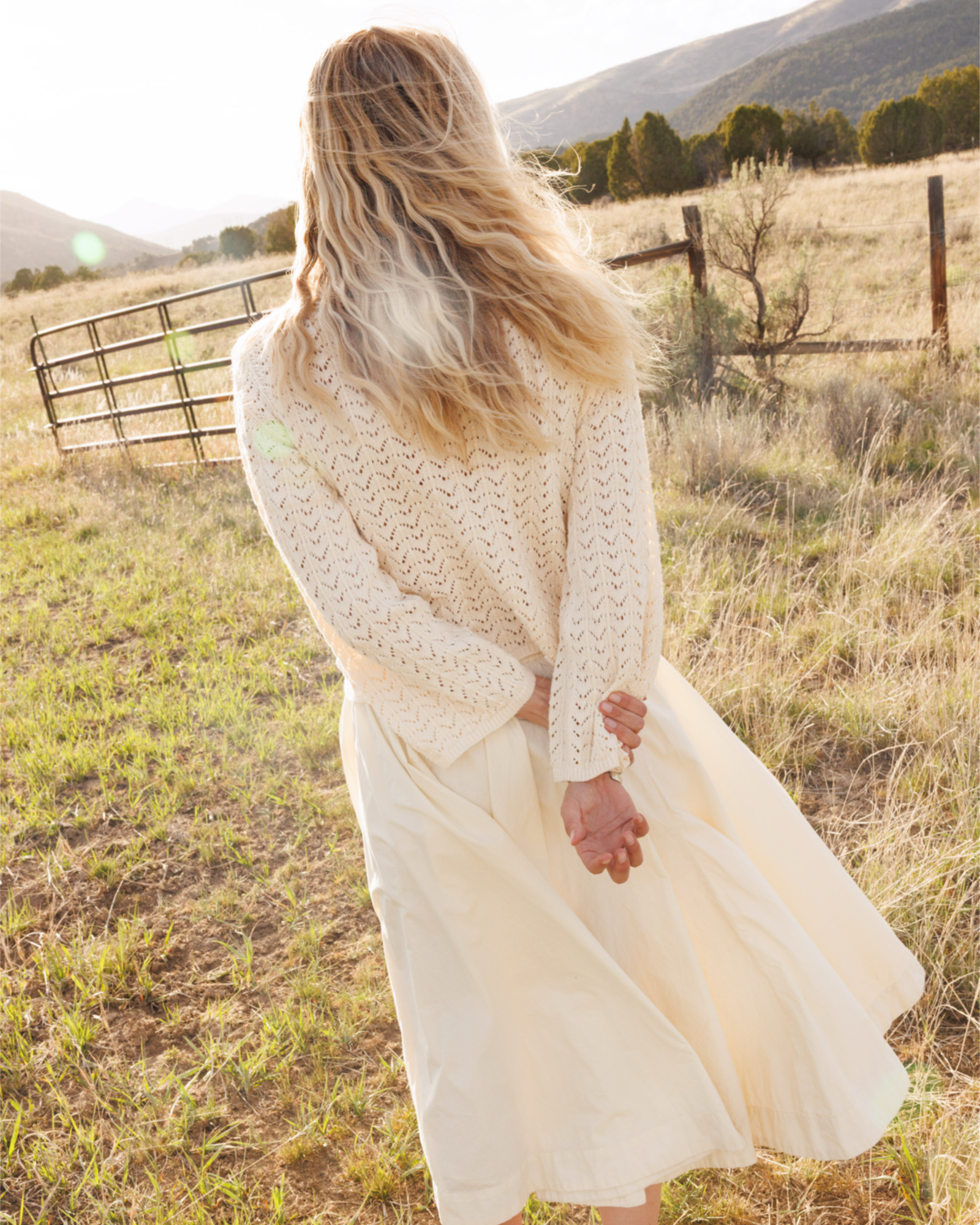 Woman wearing a cream-colored crochet knit wearing and a cream-colored skirt in a field outdoors.