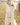 Woman in a crochet knit skirt and cotton skirt standing by a wooden fence in a field.