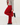 A person wearing bright red pleated wide-leg pants with a gathered ruffle hem, styled with a gray cropped cardigan and black leather loafers, standing on a white wooden floor against a white wall.