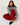 A woman sits on white wooden floorboards wearing a gray knit sweater with iridescent buttons, red pleated pants, and black tassel loafers.
