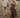 Woman in a brown outfit leading a white horse in a field with mountains in the background.