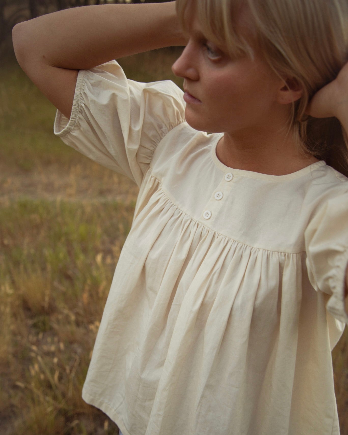 Woman standing outdoors wearing a cream babydoll-style blouse with short balloon sleeves.
