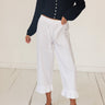 A model wearing white pants with ruffled hems, paired with a navy blue long-sleeve button-front cardigan and black flats, standing on a white wooden floor against a white wall.