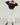 A woman modeling a navy blue button-up cardigan and white wide-leg pants with ruffled hems, paired with black flats, in a bright studio setting with white wooden floors.