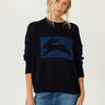 A woman modeling a dark navy blue knit sweater with a large blue rectangular panel on the chest featuring a black rabbit silhouette, paired with a denim mini skirt against a plain light background.