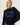 A woman wearing a dark navy blue knit sweater with a large blue rectangular panel on the chest featuring a black rabbit silhouette, paired with blue jeans against a plain off-white wall.