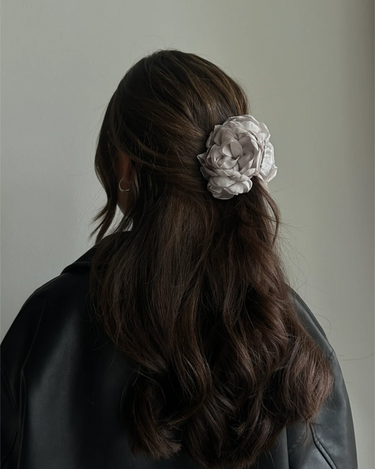 Woman with long dark hair wearing a floral hair accessory against a neutral background