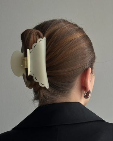 Person wearing a large matte cream hair clip on a plain background