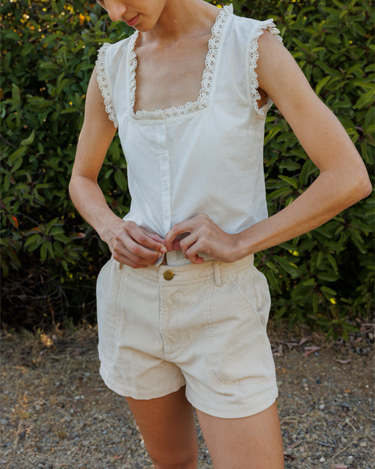 Person wearing a white sleeveless top and beige shorts outdoors.