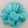 A single artificial flower embellishment in a vibrant turquoise or light blue-green color, made from layered sheer fabric petals, shown on a plain light beige background.