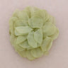 A single pale olive green fabric flower accessory, made of layered sheer petal-like ruffles, centered on a solid light pink background.