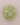 A single pale olive green fabric flower accessory, made of layered sheer petal-like ruffles, centered on a solid light pink background.