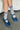 Person wearing gray socks with red and blue stripes and blue shoes on a concrete floor.
