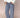 Woman wearing a white cable knit sweater and navy blue and white gingham pants on a beige background.