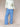 Woman wearing a white cable knit sweater and blue gingham pants on a beige background