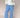 Woman wearing a white cable knit sweater and blue gingham pants on a beige background