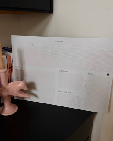 Weekly planner sheet on a shelf with books and a decorative item.