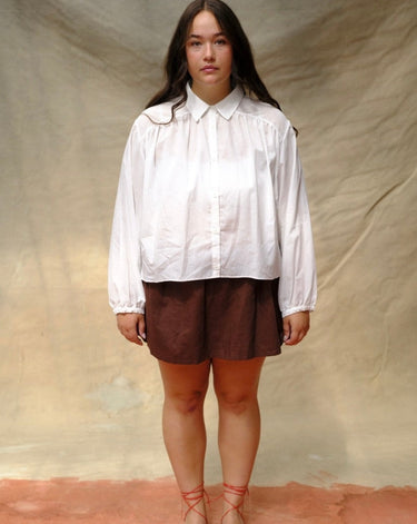 Woman wearing a white blouse and brown skirt against a beige background.