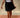 Close-up of a woman wearing a thin strap tank top and black skirt with black loafers against a beige background.