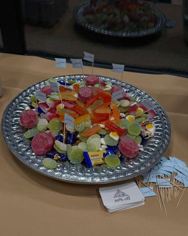 Metal tray with colorful candies and small flags on a beige surface.