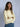 A woman wearing a butter yellow sweater and blue jeans, standing against a plain background.
