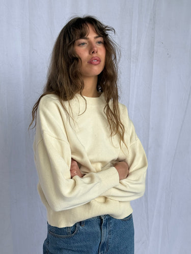 A woman wearing a butter yellow sweater and blue jeans, standing against a plain background.