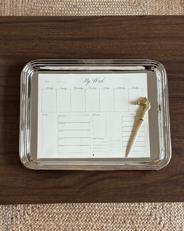 Silver tray with a planner sheet and gold pen on a wooden surface