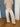 Woman wearing a beige knit cardigan and yellow striped pants standing in front of a blue door inside.