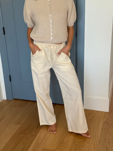 Woman wearing a beige knit cardigan and yellow striped pants standing in front of a blue door inside.