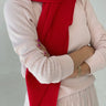 Person wearing a red scarf and beige sweater against a plain background