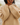 A close-up of a person wearing a chunky knit sweater in a warm camel beige color, standing outdoors near a body of water.